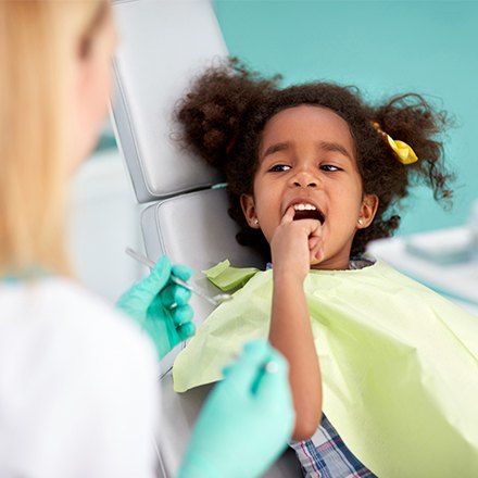 Little girl in dental chair pointing at her tooth