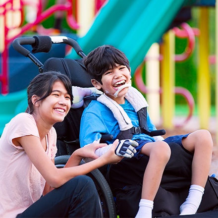 Young woman and a young man in wheel chair laughing together outdoors