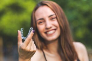 Girl with purple nails holding out clear aligner